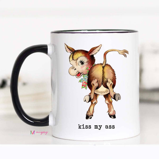 A white ceramic coffee mug with a black rim and handle, featuring a double-sided print of a donkey with a flower in its mouth and the phrase 'KISS MY ASS' on the other side.